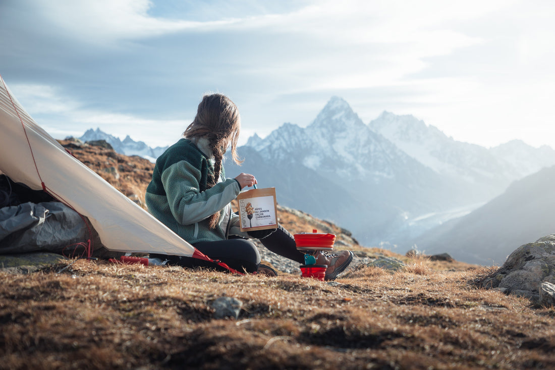 Randonneuse préparant un repas lyophilisé en bivouac face aux montagnes lors d’un trek outdoor